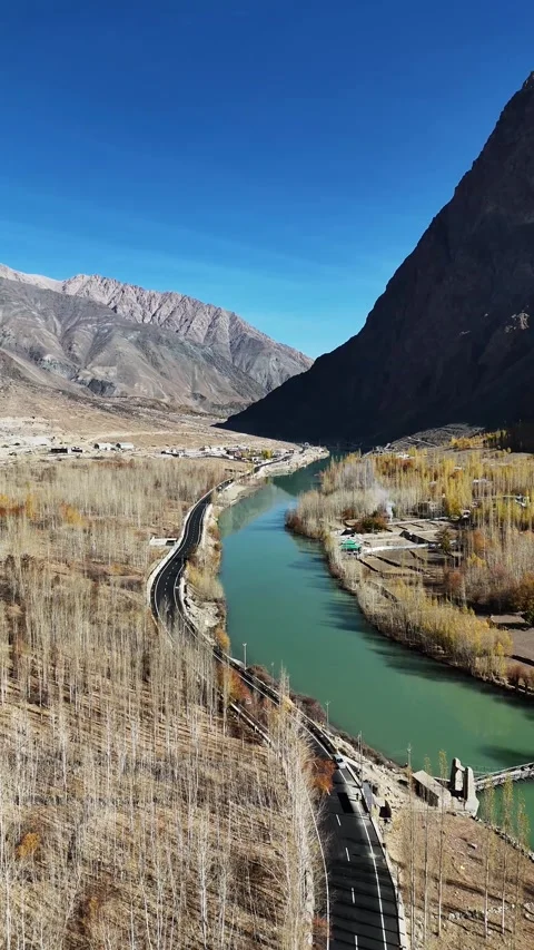 Vertical drone flyover of autumn trees flanking road and flowing river. Stock Footage 310662219