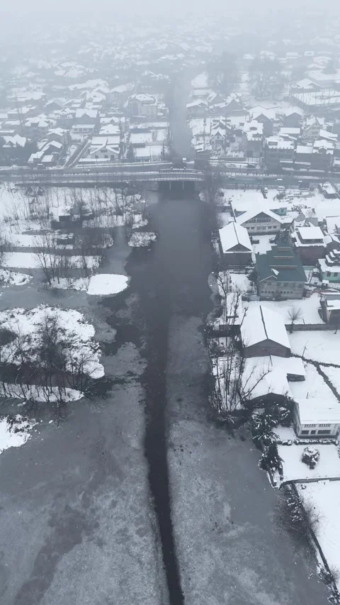 Vertical drone footage capturing the peaceful snowfall over Dal Lake's waters. Stock Footage 311021799