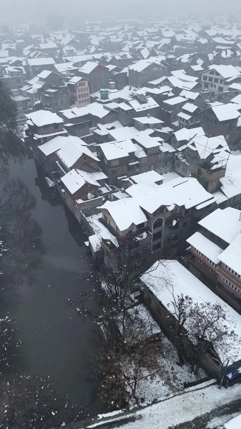 Vertical drone footage flying over tightly packed snowy rooftops with winter Stock Footage 311021379
