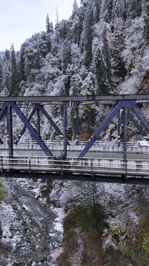 Vertical drone footage showcasing a parallel ride over a draped bridge in a snow Video stock 311151301