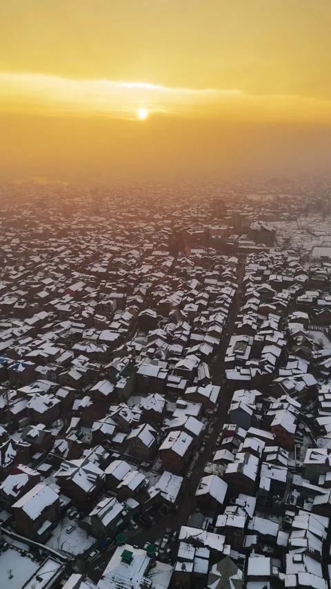 Vertical drone footage of snow-covered rooftops glowing at sunset. Stock Footage 311021455