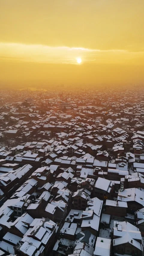 Vertical drone footage of sunset glow softly illuminating the snowy rooftops. Stock Footage 311021856