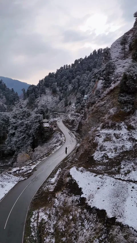 Vertical drone footage tracking a biker on a snow-covered Mughal Road winding Stock Footage 311151548