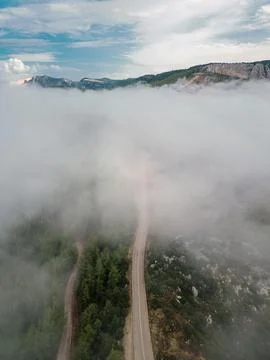 Vertical drone image of a winding mountain road emerging through clouds Stock Photos