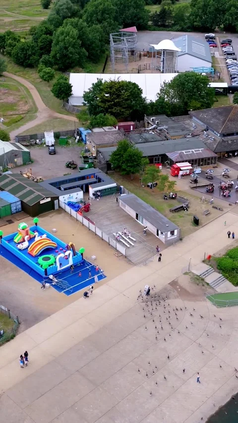 Vertical drone orbit of Fairlop Waters, car park, café, bouncy castle, boats Stock Footage 312793835