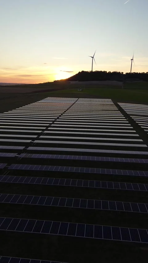 Vertical Drone Pullback from Solar Panels with Wind Turbines at Sunset Stock Footage 330453596