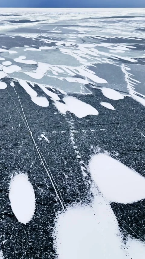 Vertical drone shot over dark Baltic Sea ice with scattered snow patches and a Stock Footage 332241455