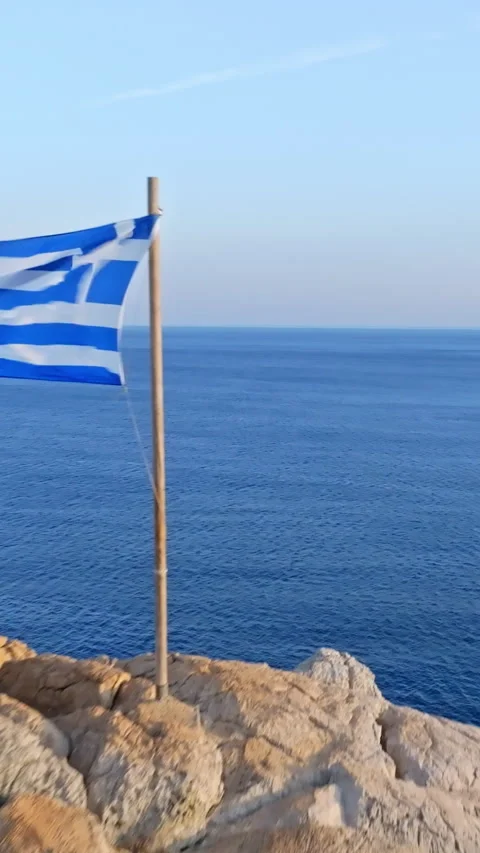 Vertical drone shot passing a Greek flag on coastal cliffs in Greece, sunset Stock Footage 320164883