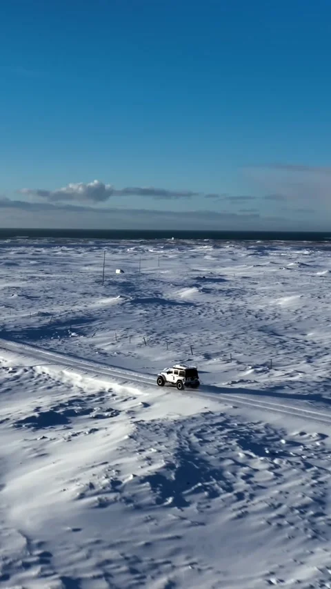 Vertical drone shot of a white 4x4 crossing the frozen plains of Kleifarvatn Vidéo 334581323