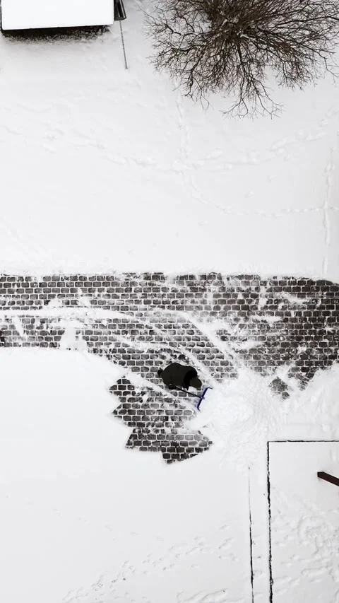 Vertical drone top-down shot of a worker pushing a shovel to clear fresh snow Stock Footage 328872142