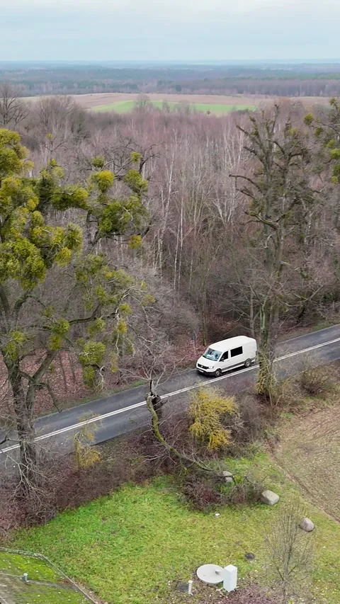 Vertical Drone Tracking Shot of White Camper Van Driving on Rural Road Stock Footage 323877465