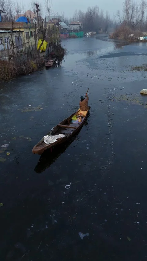 Vertical drone trailing the cold journey of a boatman across Dal Lake’s snowy Stock Footage 311020111