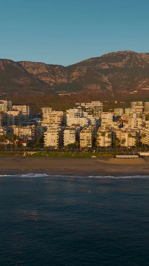 Vertical drone view of coastline with small waves and golden light at sunset Video stock 341880259