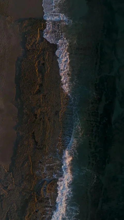 Vertical drone view of gentle waves rolling toward sandy beach at sunset Stock Footage 341875404