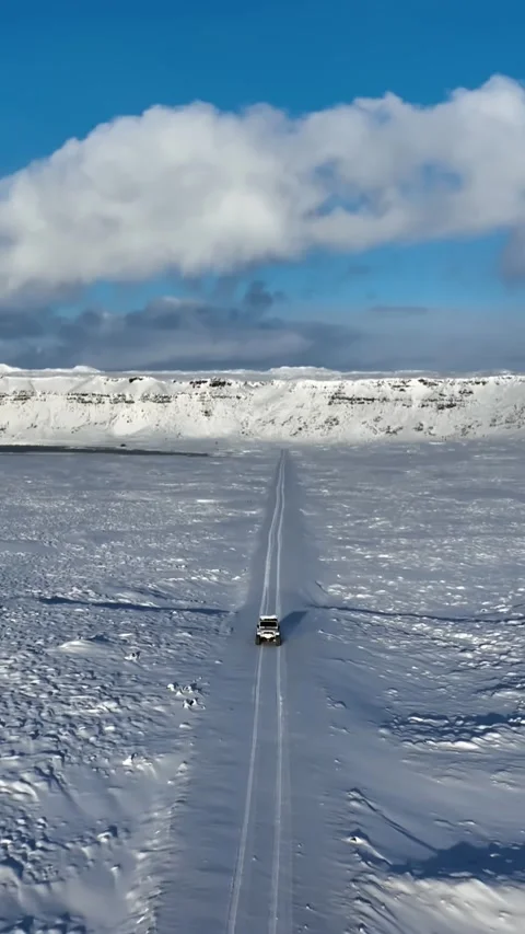Vertical drone view of a lone 4x4 cutting across the frozen expanse of Stock Footage 334582208
