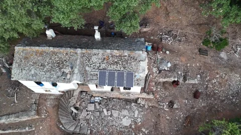 Vertical drone view of an old stone building with solar panels on a hillside. Video stock 327672103