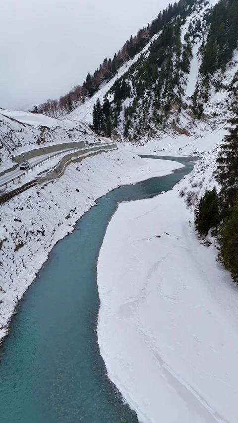 Vertical drone view of a snow-covered valley, a turquoise river, and a frozen Stock Footage 311019409