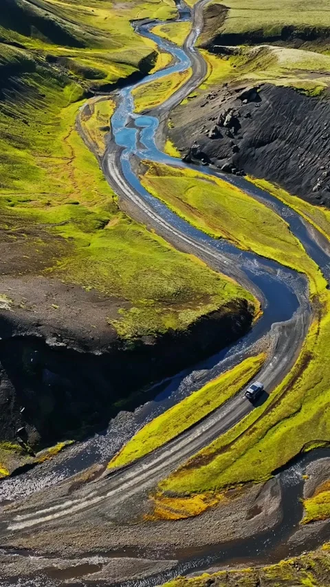Vertical drone view of a winding river cutting through green moss and dark Stock Footage 328265670