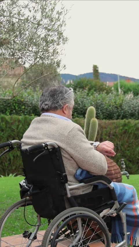 Vertical Elderly man checking wrist watch in wheelchair, enjoying garden view Stock Footage 300172236
