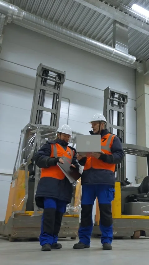 Vertical of Engineers stand in terminal of warehouse looking in laptop Stock Footage 275619649