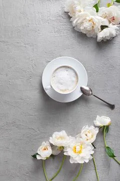 Vertical flat lay of a coffee cup with white peonies on a grey background Stock Photos