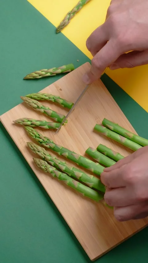 Vertical flat lay video: the cook cuts raw asparagus on the wooden board Video stock 179937492