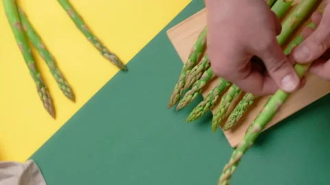 Vertical flat lay video: the cook cuts raw asparagus on the wooden board Video stock 183566735