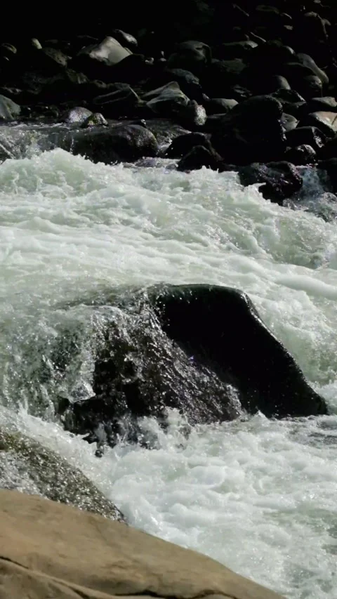 Vertical footage of a clear mountain river flowing rapidly through river rocks Video stock 320922630