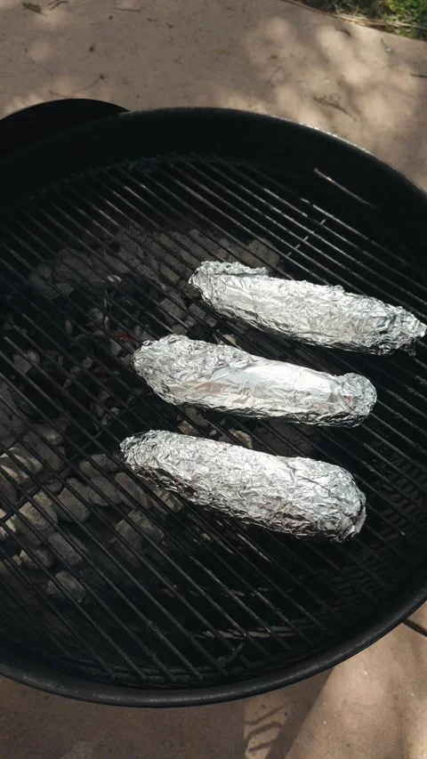 Vertical footage of corn wrapped in foil cooking on a charcoal grill Stock Footage 335598588