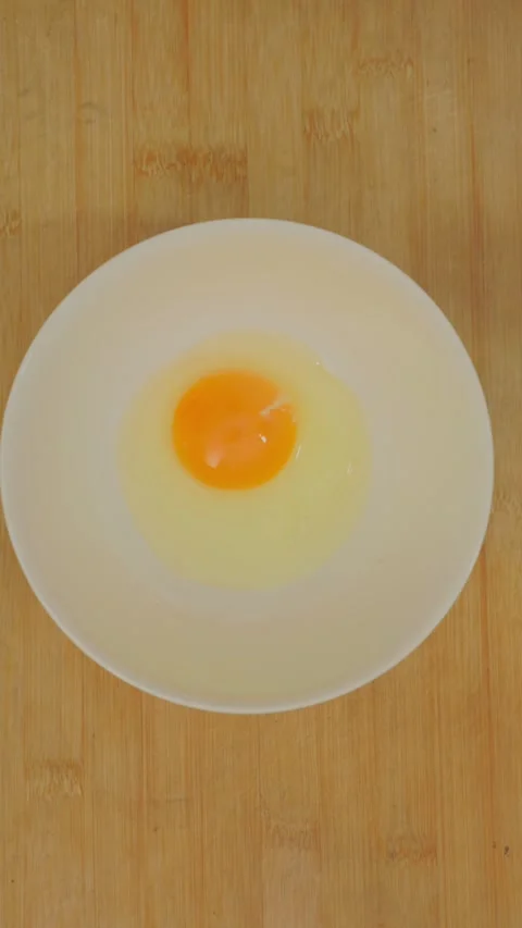 Vertical footage cracking raw egg and pouring liquid into white ceramic bowl. Stock Footage 337455081