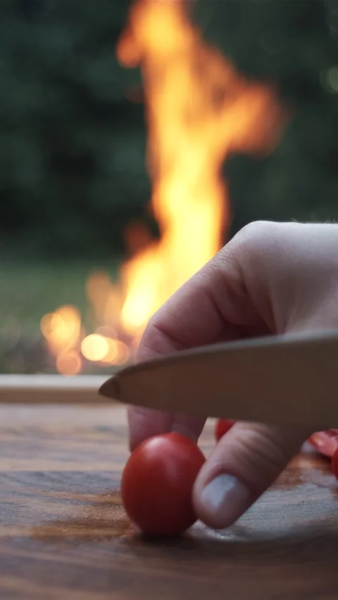 Vertical footage of female hands using knife cutting red tomato near campfire Stock Footage 284927354
