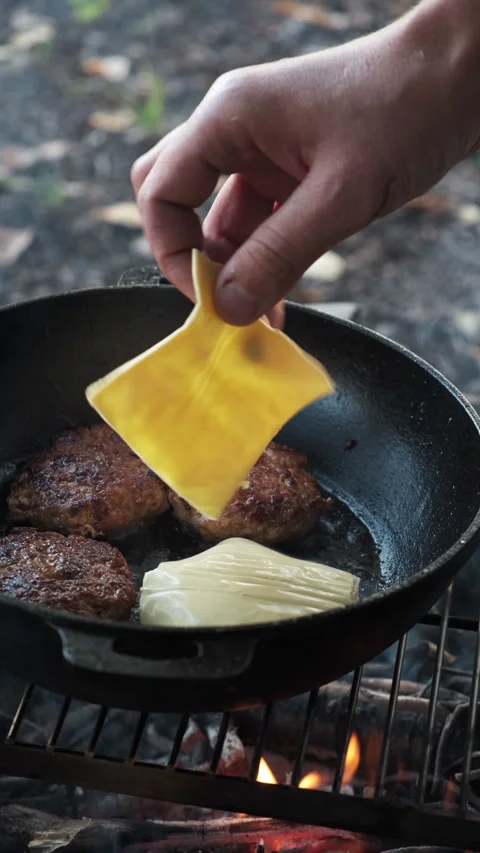 Vertical footage of hands adding cheese on meat burger cutlet on pan at outdoors Stock Footage 286311610