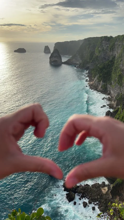 Vertical footage of hands making a heart shape over turquoise ocean and dramatic 스톡 동영상 335834536