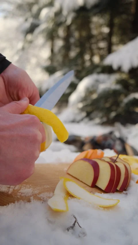 Vertical footage of man peeling lemon for mulled wine on background bonfire Stock Footage 300939730