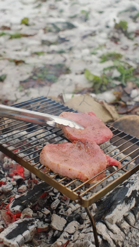 Vertical footage of man put beef steaks metal grid on bonfire at winter day Stock Footage 297944000