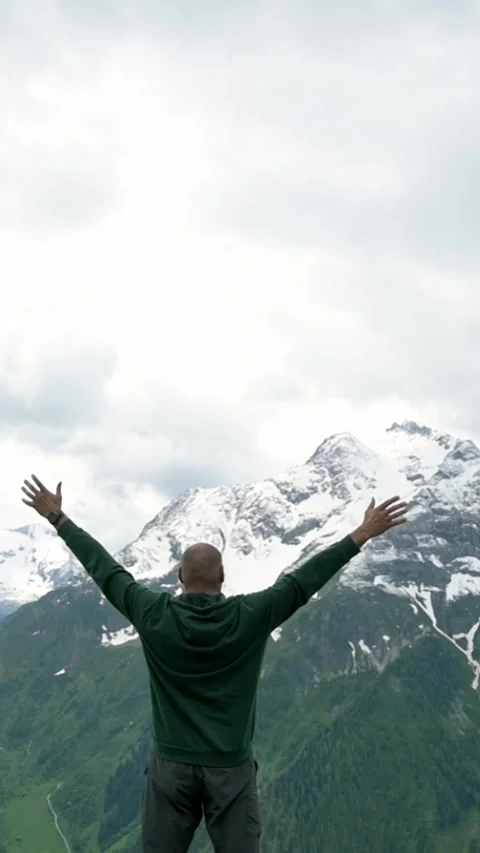 Vertical footage of a man standing with arms raised in triumph, facing snow Видео 287934853