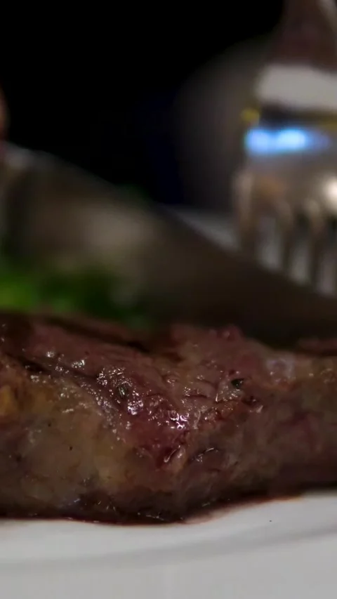 Vertical footage of Process of cutting the steak with a large kitchen knife on a Stock Footage 306944227