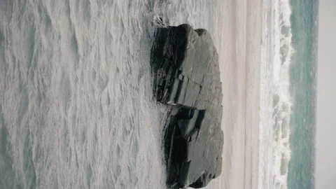 Vertical footage of rocks on the beach being hit by high tide. Video stock 169748727