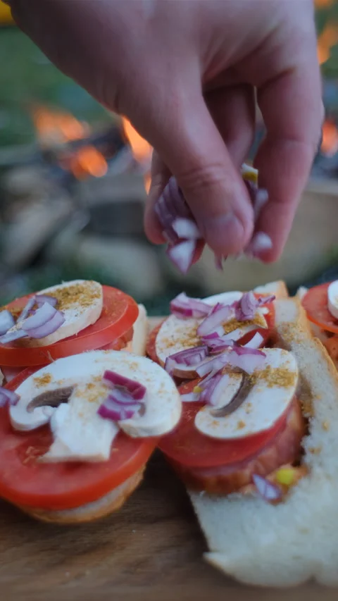 Vertical footage of unknown young man sprinkles onions on baguette near bonfire Video stock 271225231