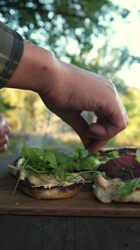 Vertical footage of unknown young man cooking tasty burger in autumn forest Stock Footage 286312494