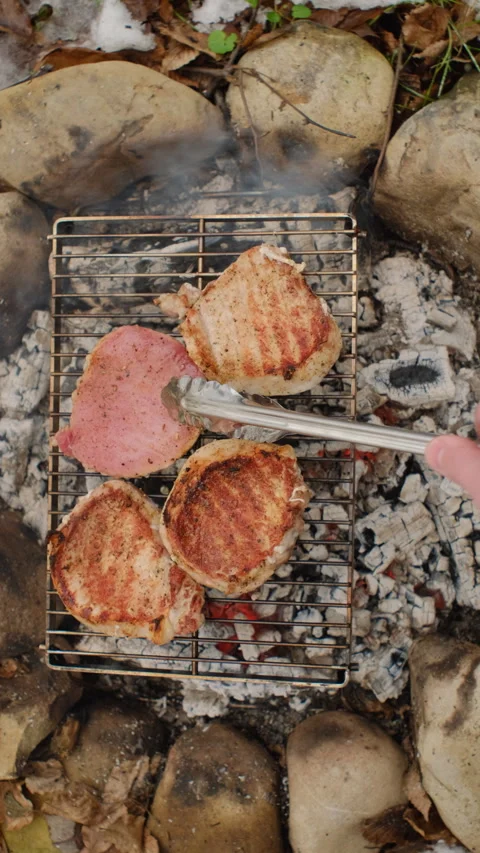 Vertical footage of unknown young man cooking beef steak metal grid on bonfire Stock Footage 297944159