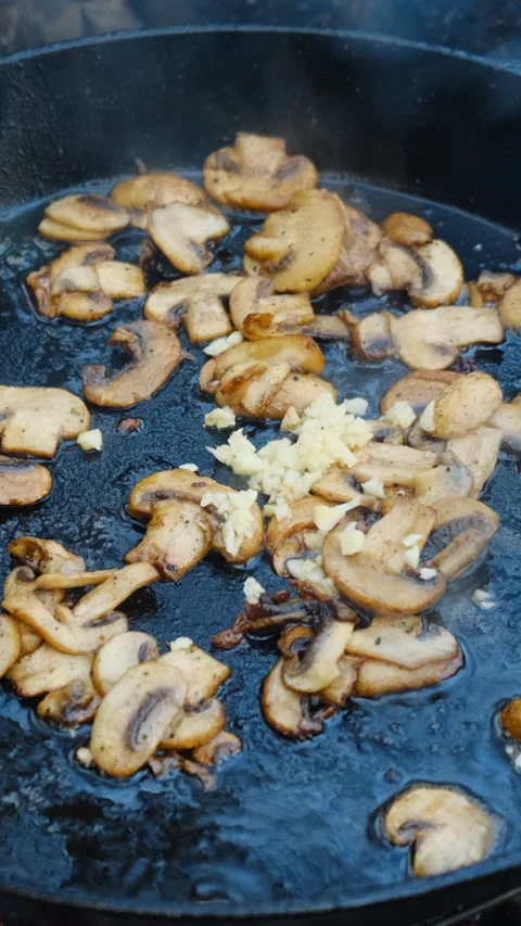 Vertical footage of unknown young man frying mushrooms in pan on bonfire Stock Footage 309031116