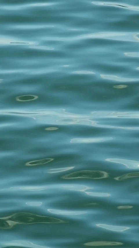 Vertical footage of waves moving with calm ripples on the surface of a blue lake Stock Footage 319968938