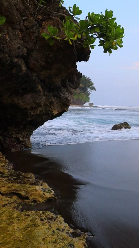 Vertical Footage of Waves Washing Onto a Black Sand Beach Beside a Rocky Cliff Stock Footage 343810556