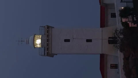 Vertical format lighthouse beacon spins in twilight blue evening sky Stock Footage 327416443