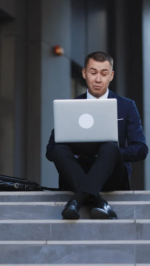 Vertical Format Video of Happy guy sitting on stairs and working outdoors. Happy Stock Footage 302805260