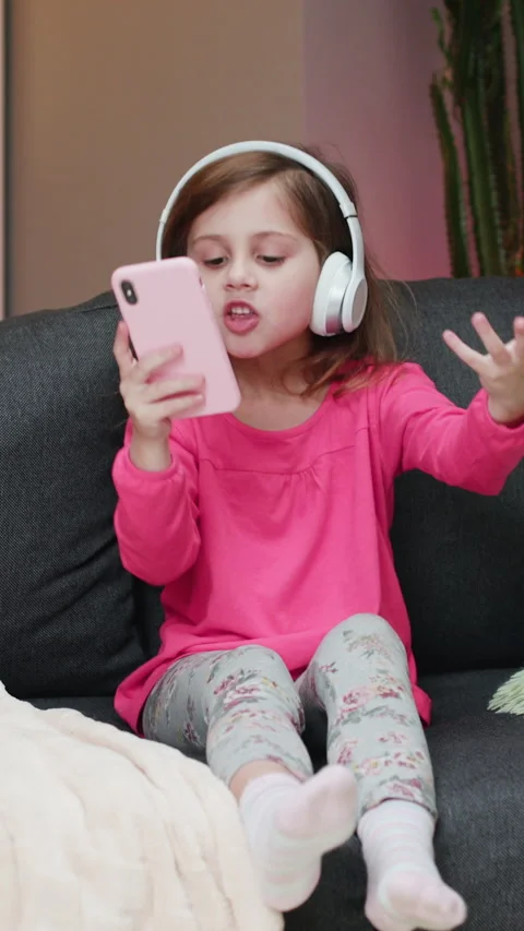 Vertical Format Video of Little joyful girl in headphones is dance on sofa and Stock Footage 303380471