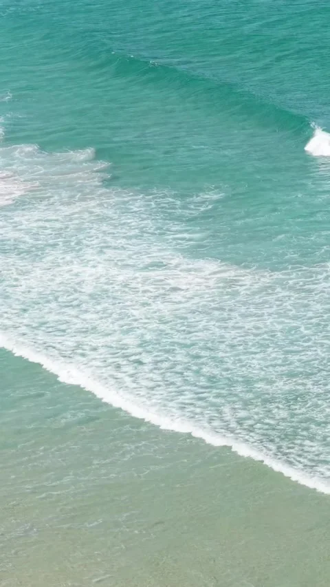Vertical format video showing turquoise waves rolling onto the sandy shoreline Stock Footage 346655275