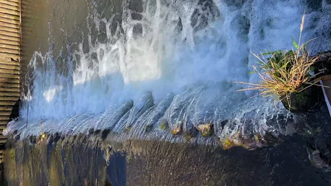 Vertical format: Water pours over small canal weir, sunny CU view Stock Footage 328527145