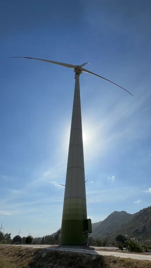 Vertical frame captures a wind turbine with blades in motion, rotating against Stock Footage 327908256